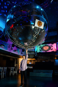 A vibrant celebration at a bar mitzvah event space, showing a crowded dance floor under a disco ball with colorful confetti raining down on the guests, creating a festive and joyous atmosphere.